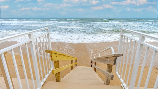Un escalier en bois menant à une plage, avec des rampes blanches.