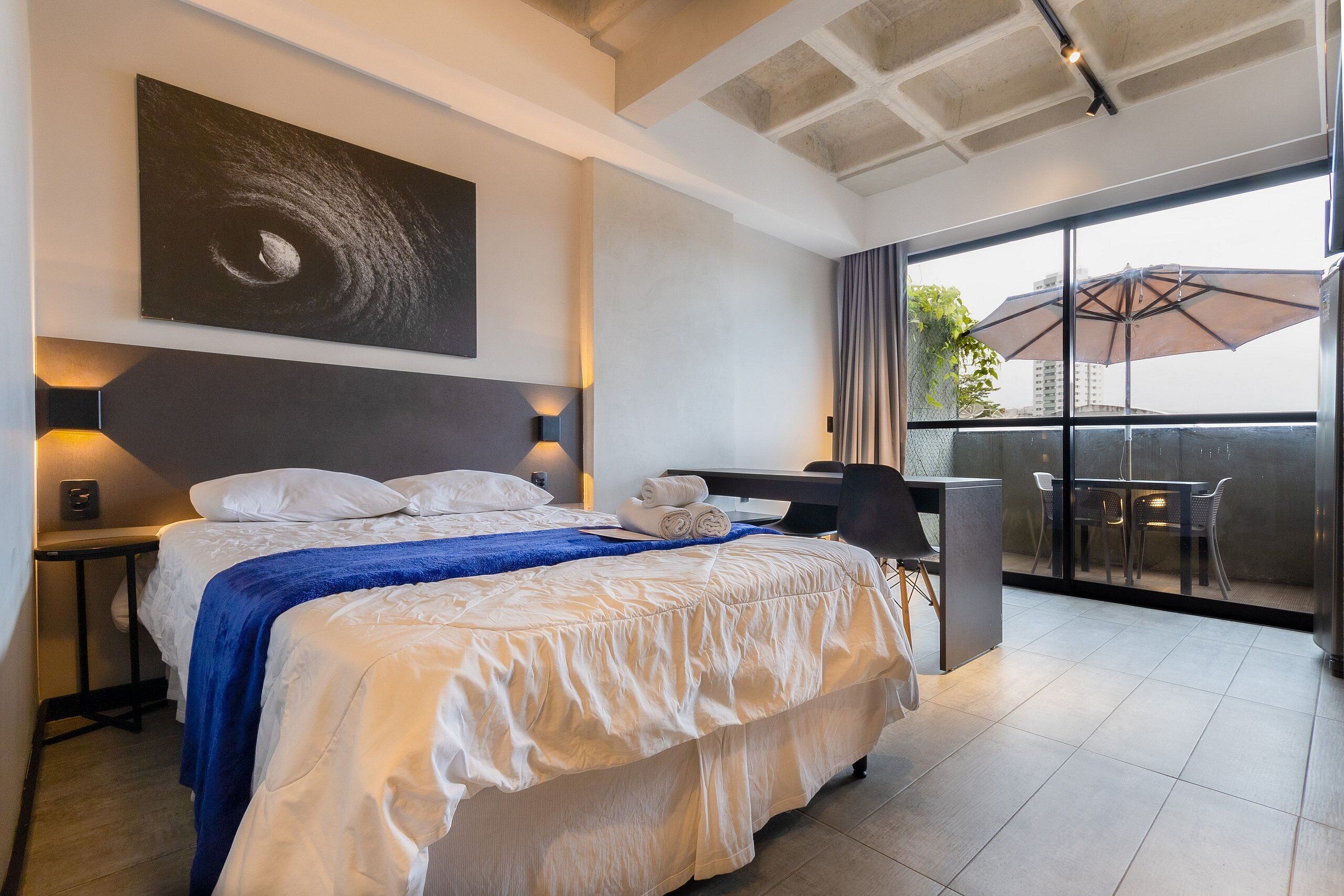 Une chambre d’hôtel avec un lit, un bureau et un balcon équipé d’un parasol.