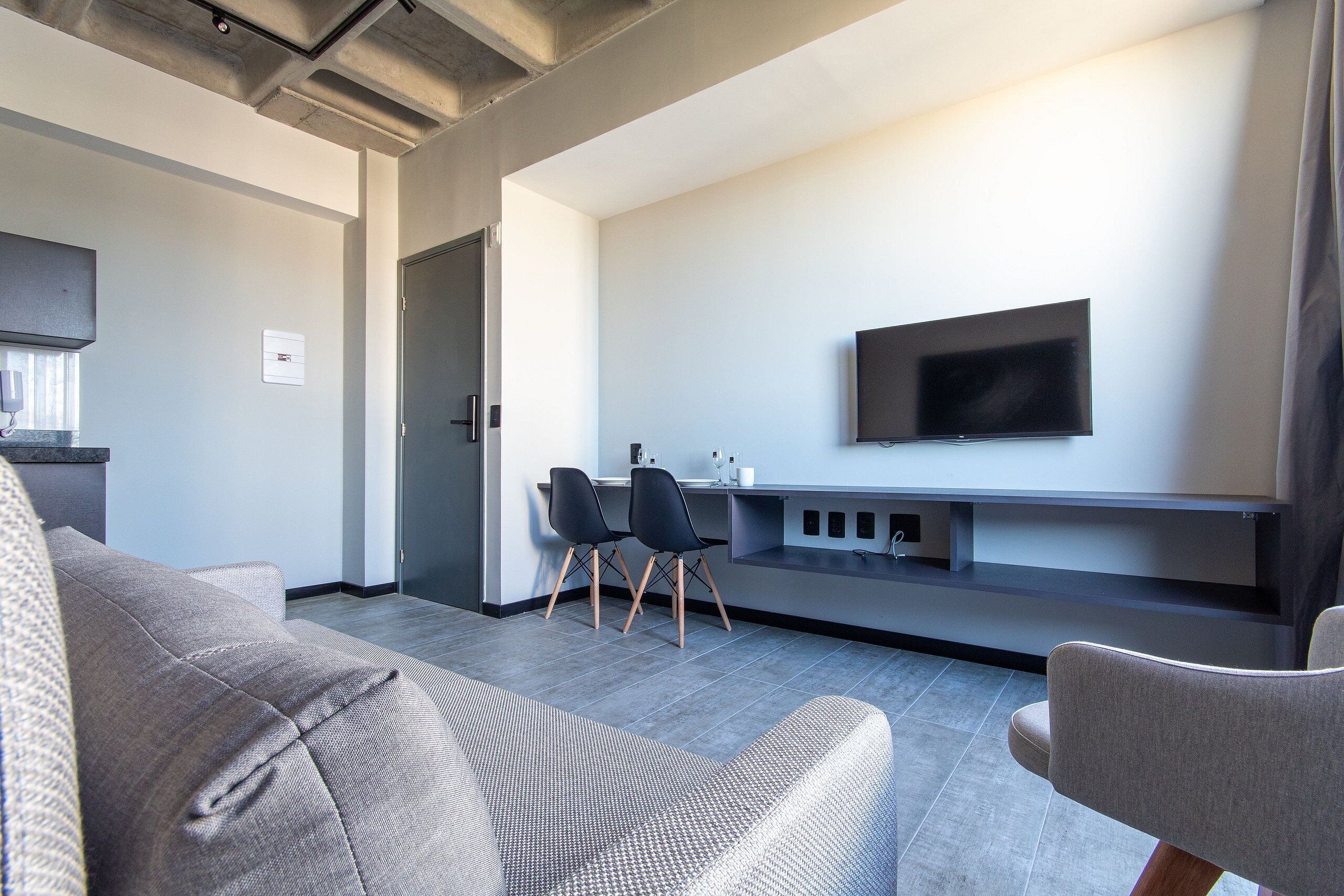 Una sala de estar moderna con un sofá y un sillón grises, y un televisor de pantalla plana montado en la pared.