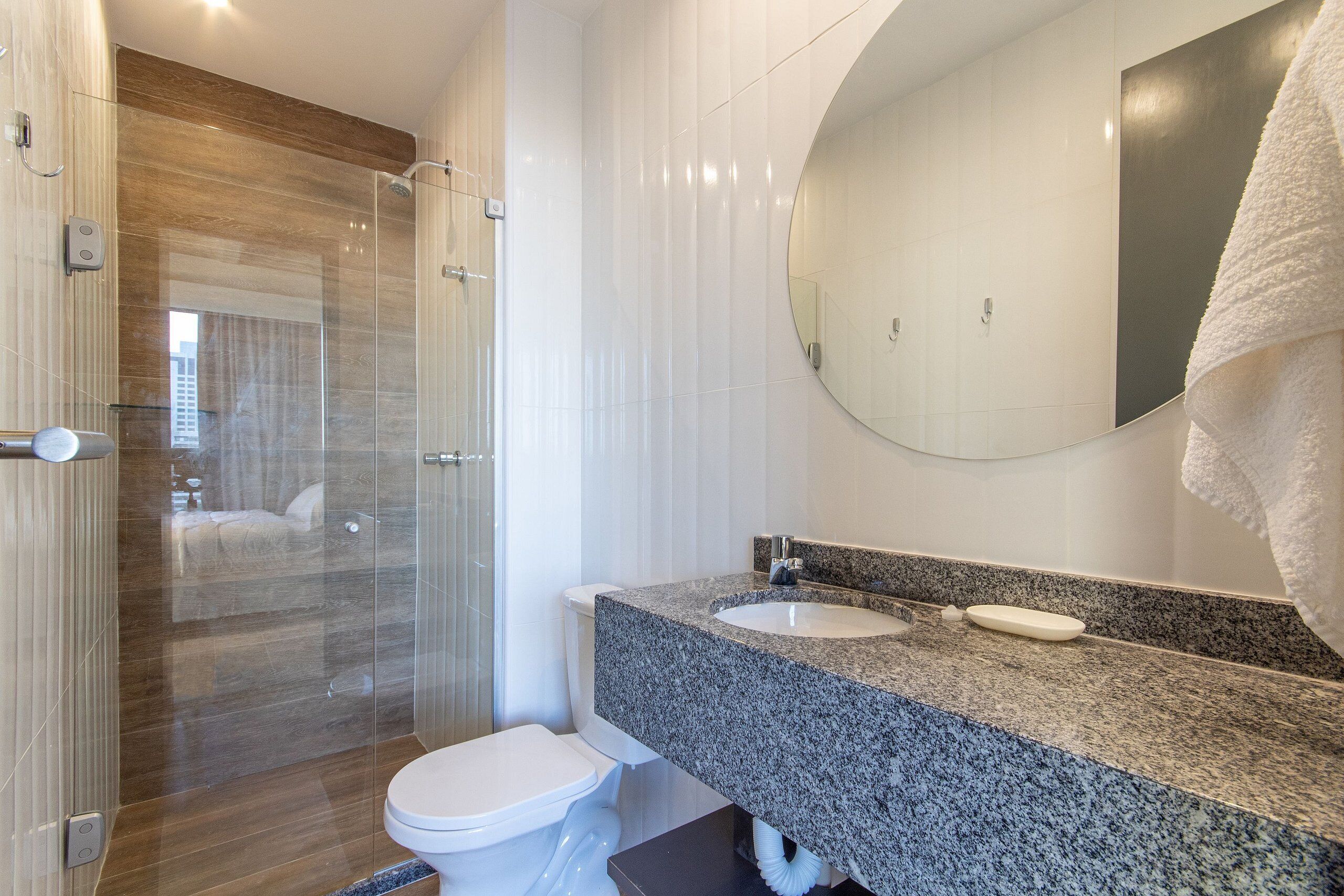 Un baño moderno con cabina de ducha de vidrio, inodoro blanco, lavabo con encimera de granito y un espejo grande.