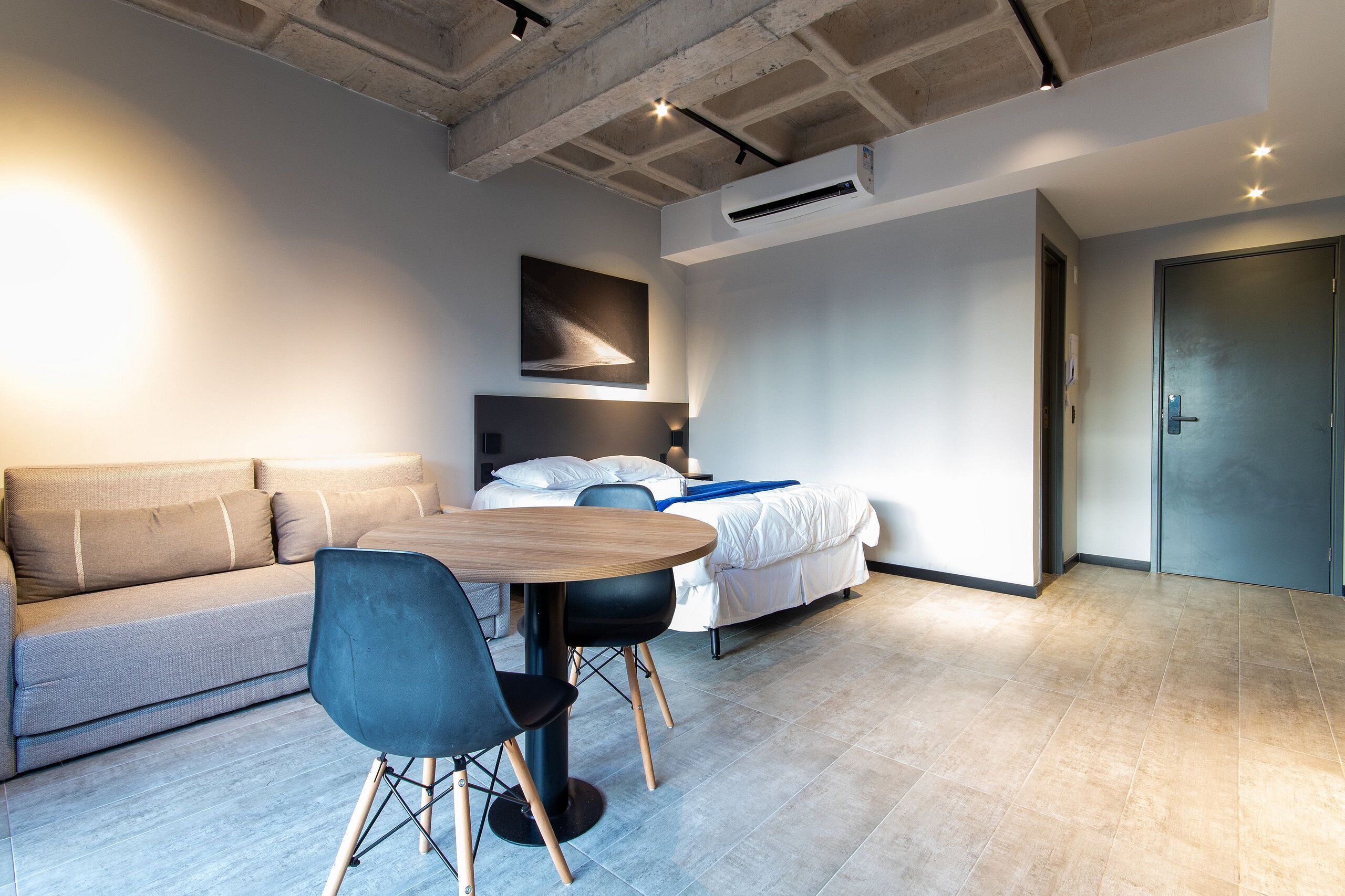 Una habitación de hotel moderna con sofá, una mesa redonda, cama y aire acondicionado.