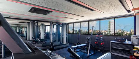 A modern gym with exercise equipment, large windows, and a city view.