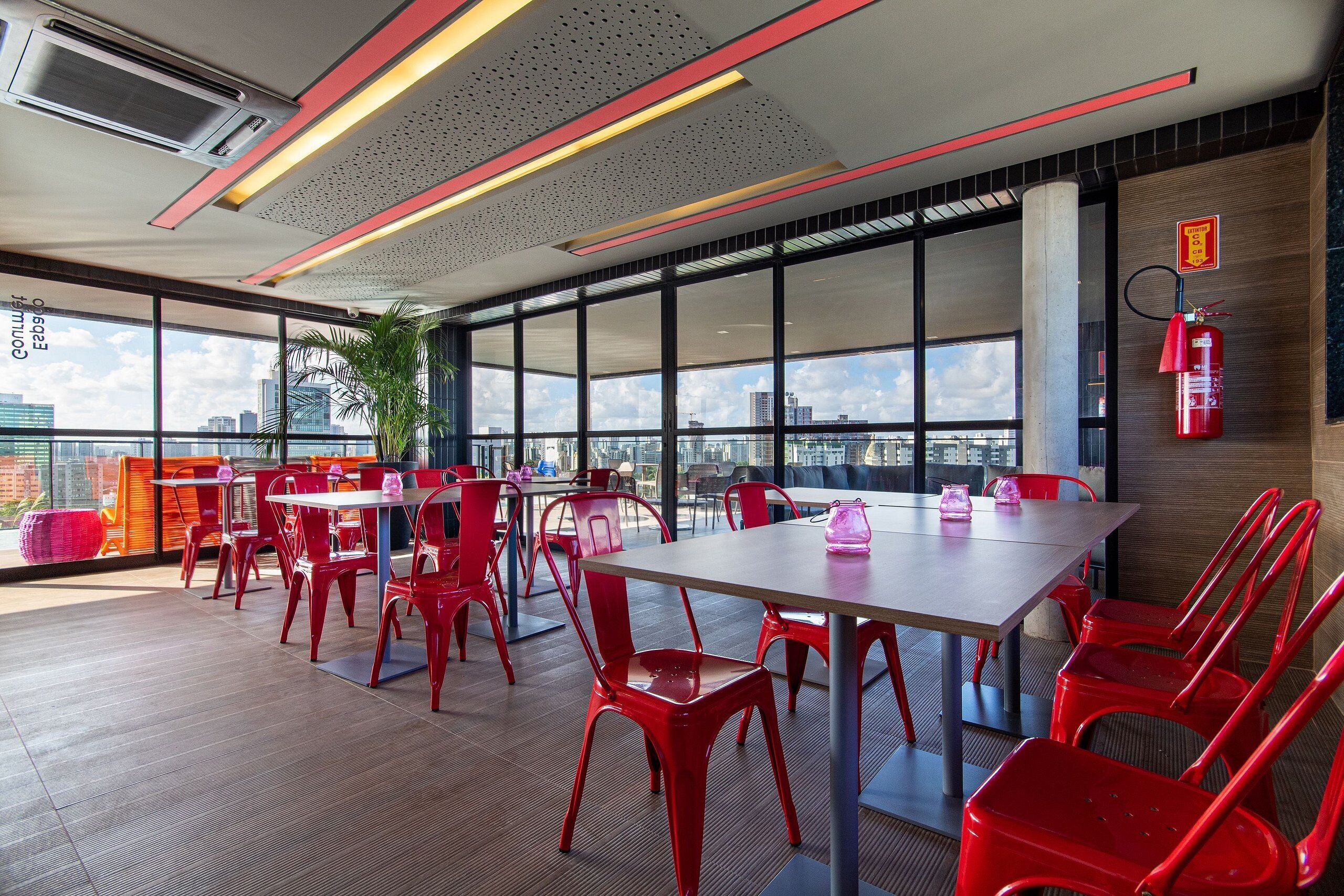Une salle de conférence moderne, dotée de chaises rouges, d’une longue table, de grandes fenêtres et offrant une vue sur la ville.