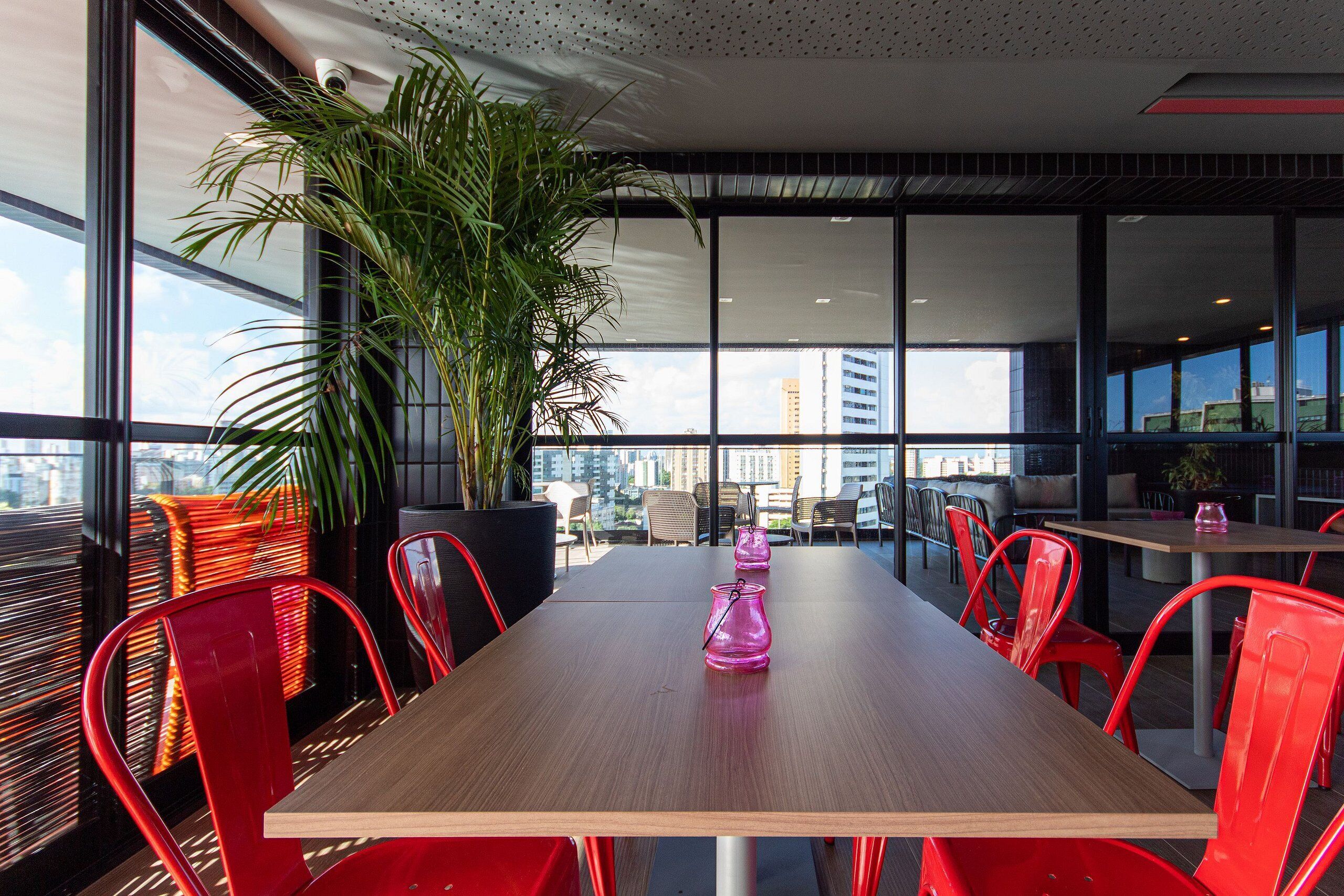 A modern dining area with a wooden table, red chairs, and a large potted plant.