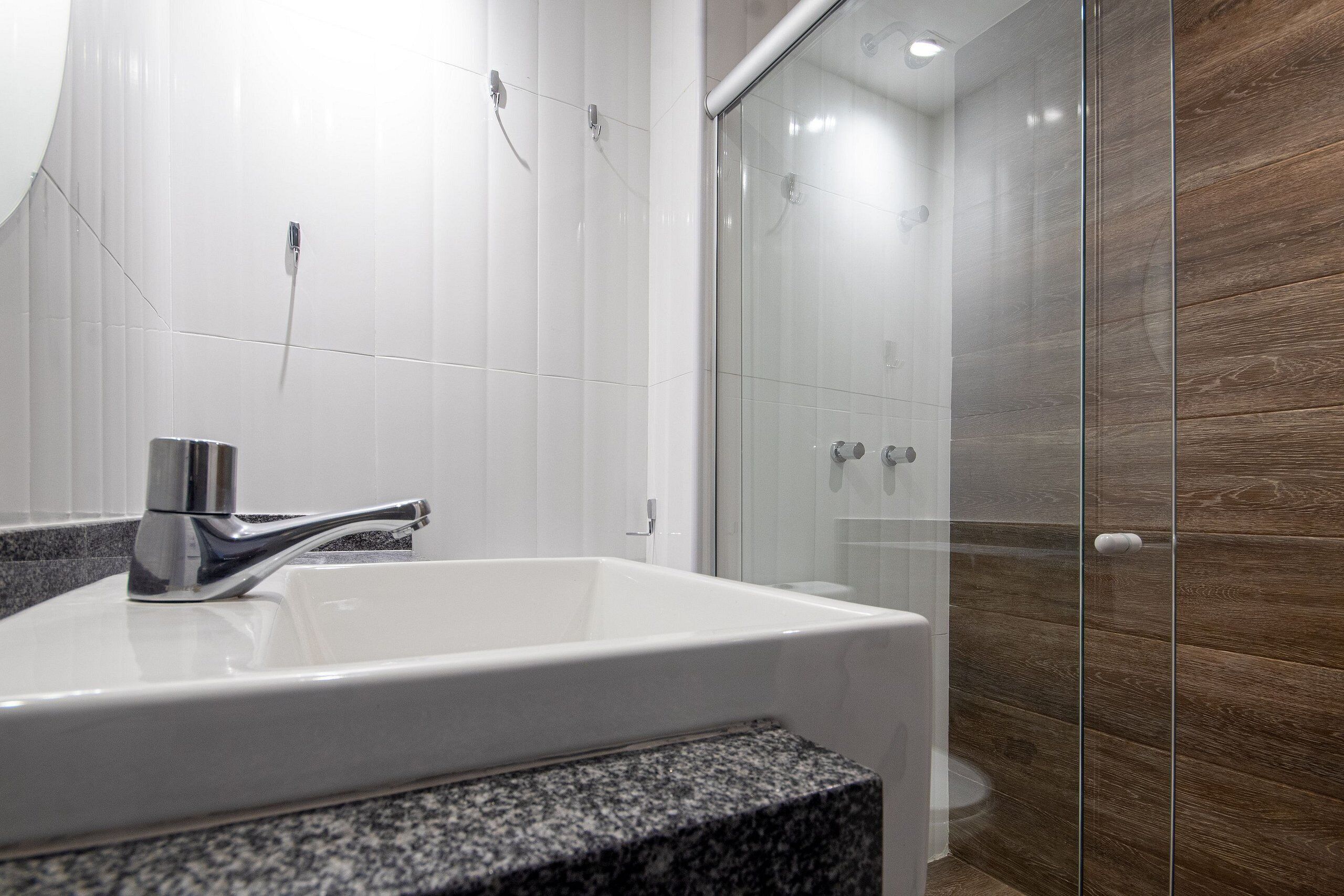 Un baño con lavamanos blanco, grifo cromado, encimera de granito y cabina de ducha de vidrio.