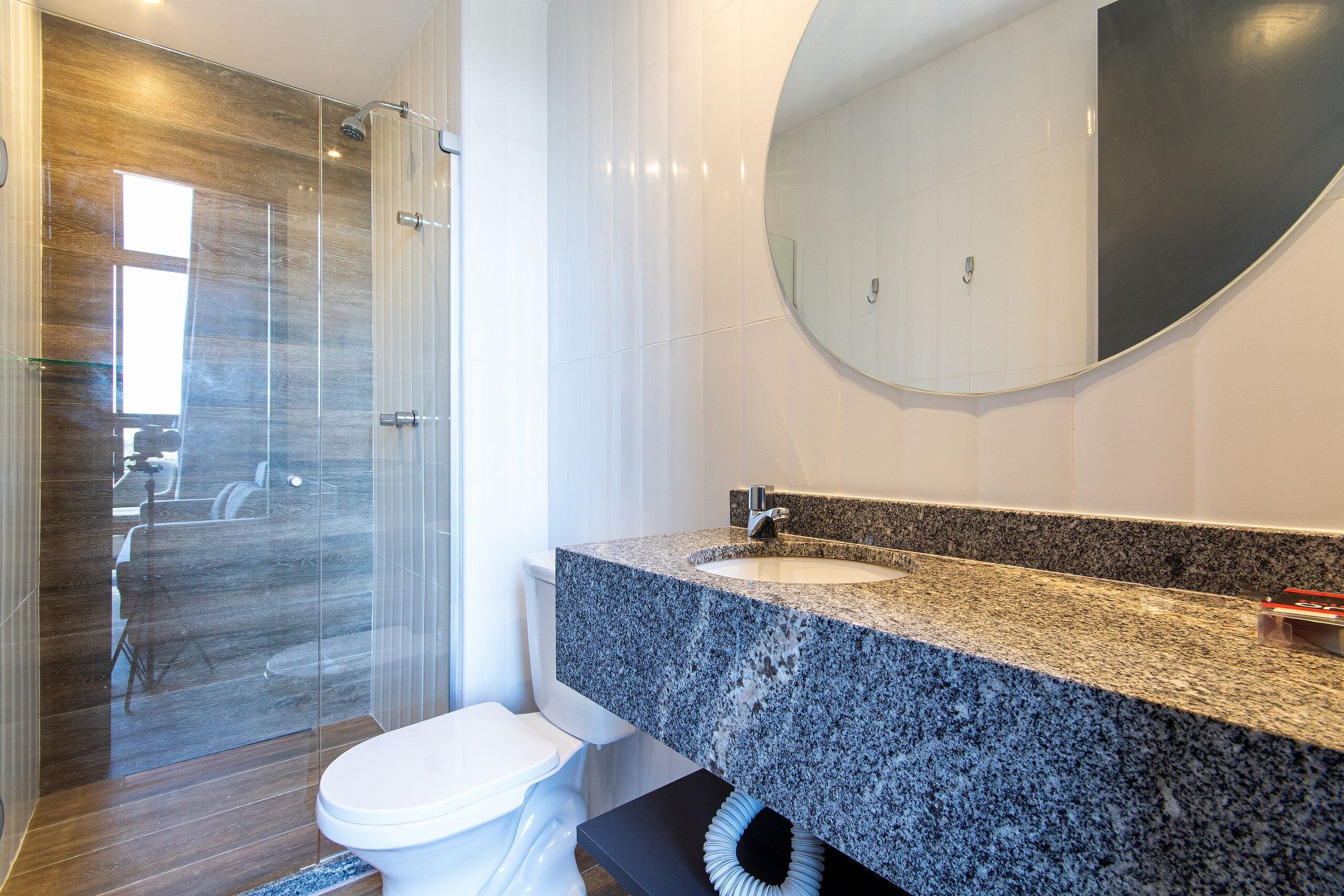 Un baño moderno con cabina de ducha de vidrio, inodoro blanco y encimera de granito con lavamanos y espejo.