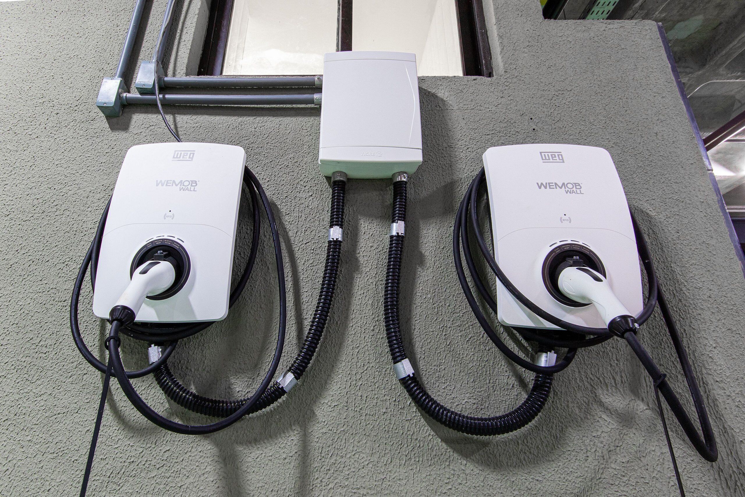 Two WEMOB WALL charging stations mounted on a textured wall, connected by a central conduit.