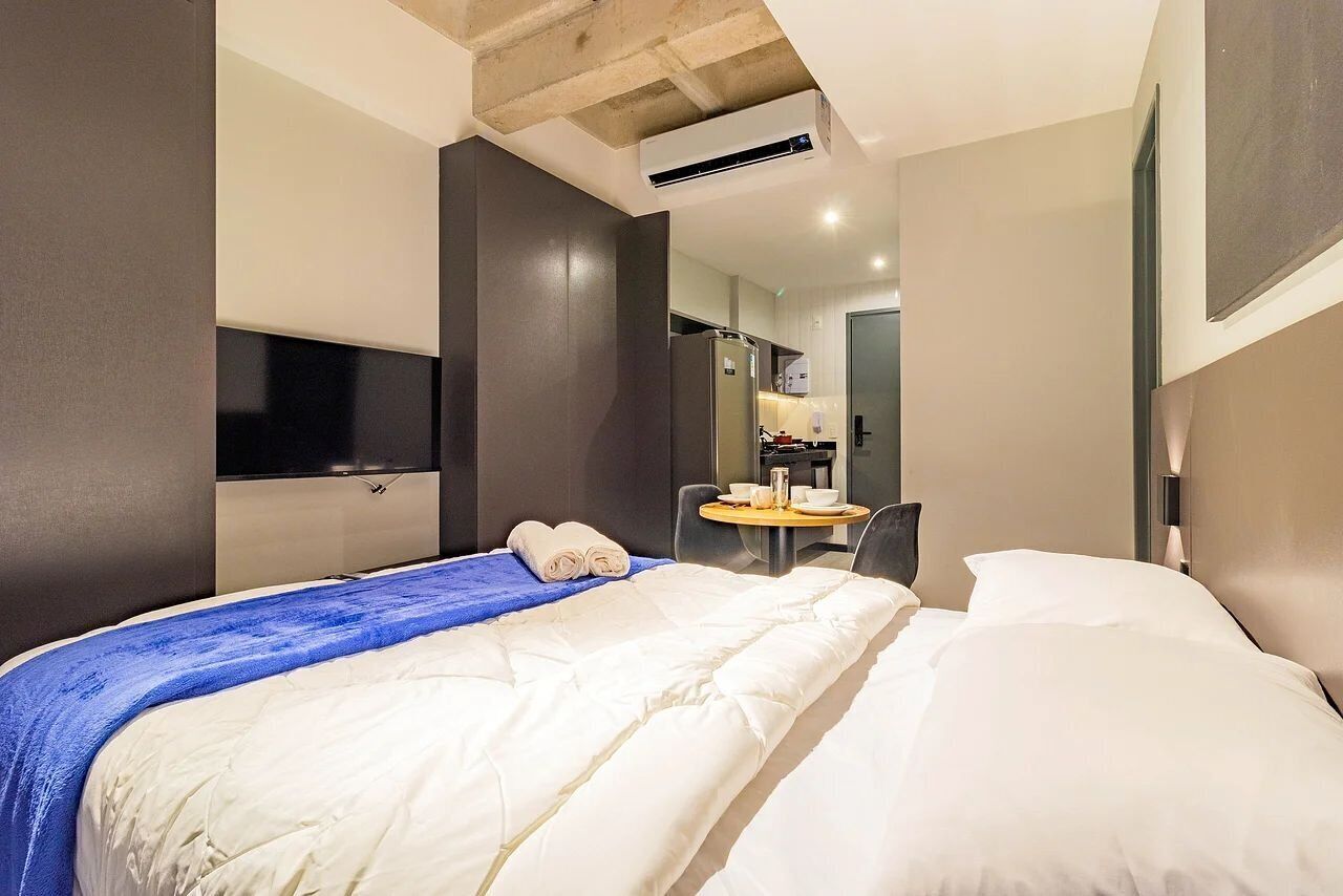 Habitación de hotel con una cama grande, un escritorio con silla, un televisor de pantalla plana montado en la pared y un equipo de aire acondicionado en el techo.