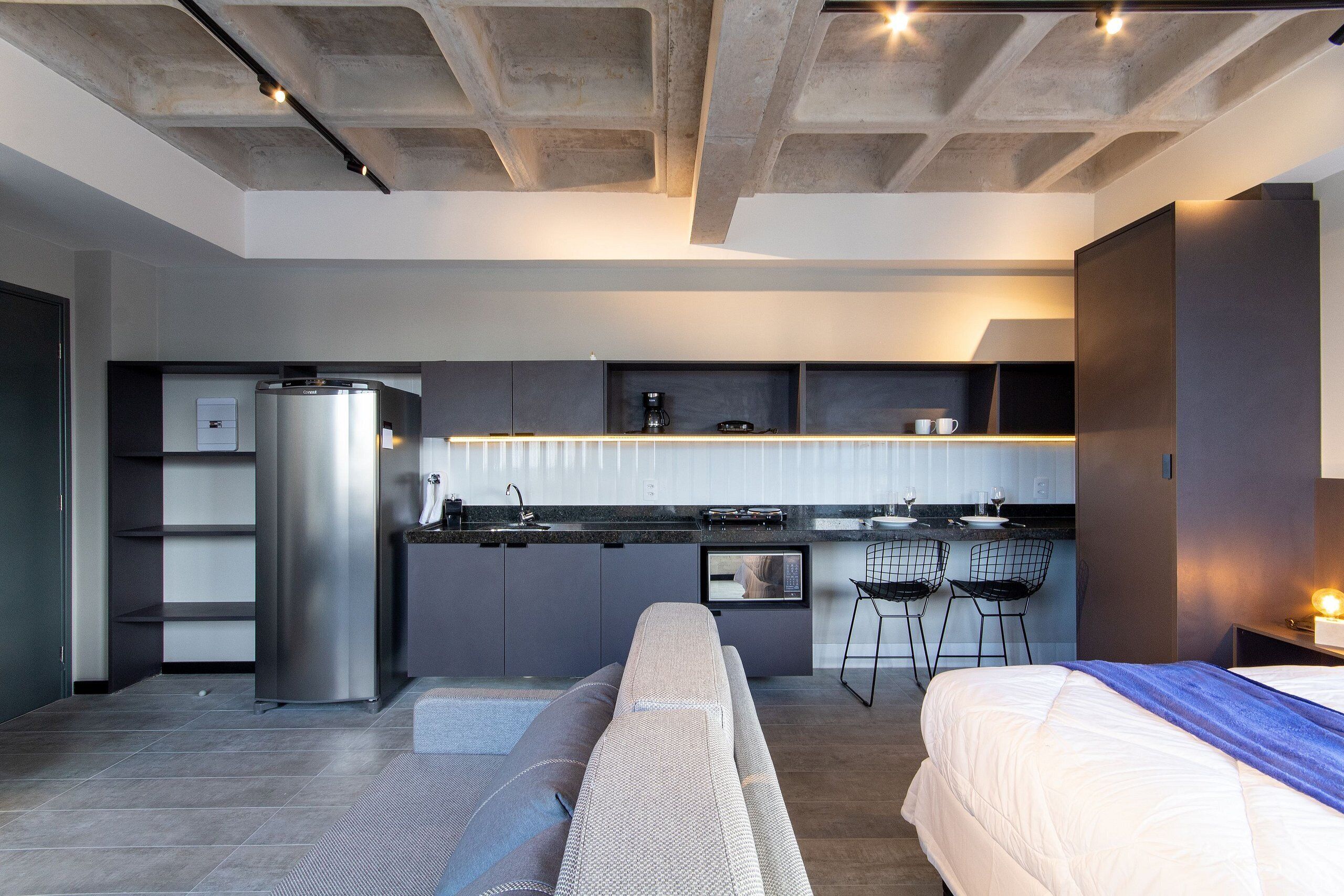 Habitació d'hotel moderna amb cuineta, un llit, un sofà i zona de menjador.