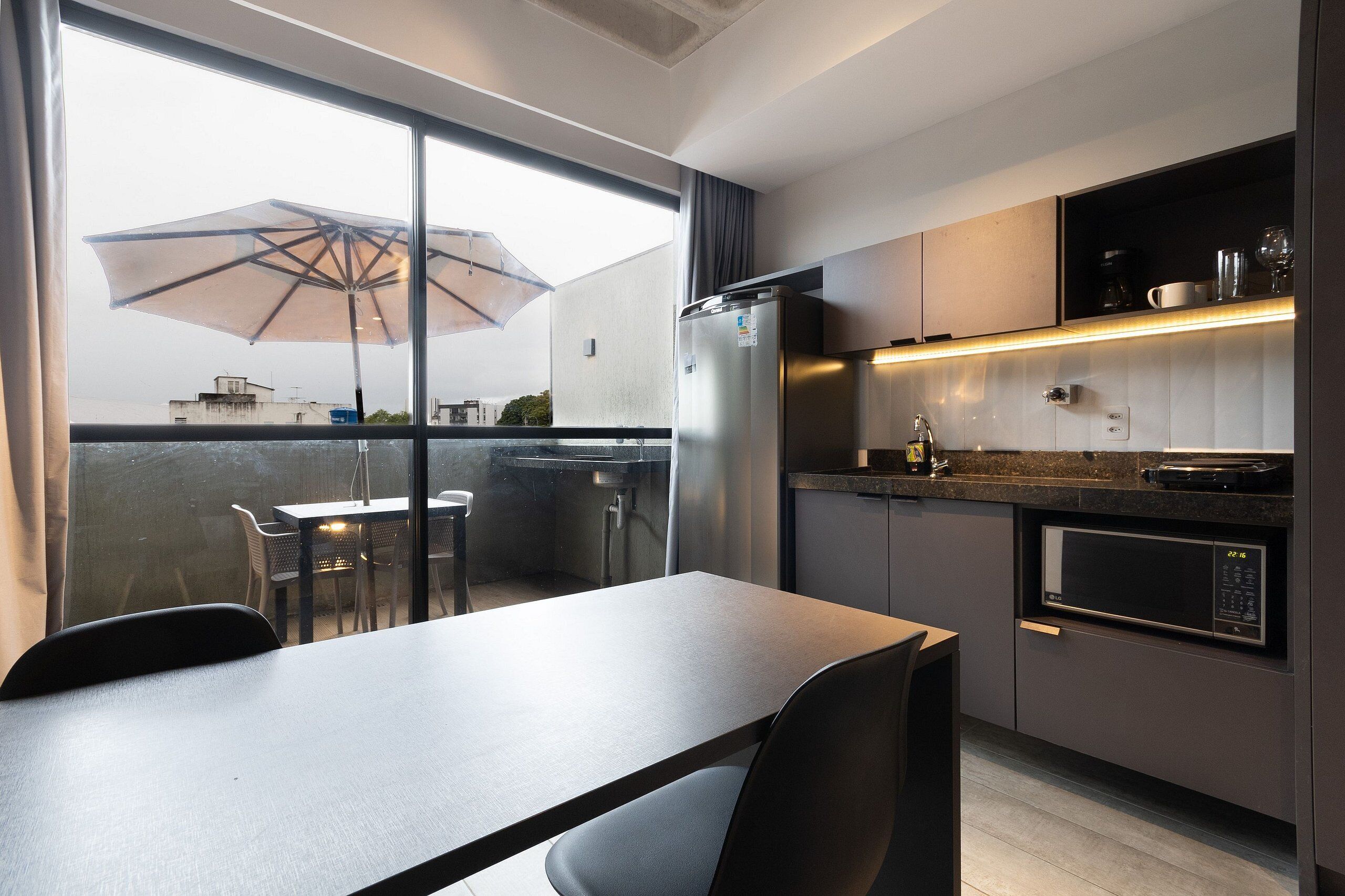 Een moderne keuken met een eethoek, een koelkast, een magnetron en een groot raam met uitzicht op een balkon.