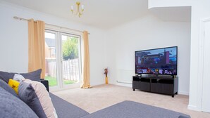 Una sala de estar moderna con un televisor de pantalla plana grande, sofás grises y un puerta corredera de vidrio que da a un jardín.