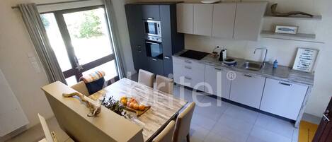 A modern kitchen with a central island, built-in appliances, and a dining area with a view of the outdoors.