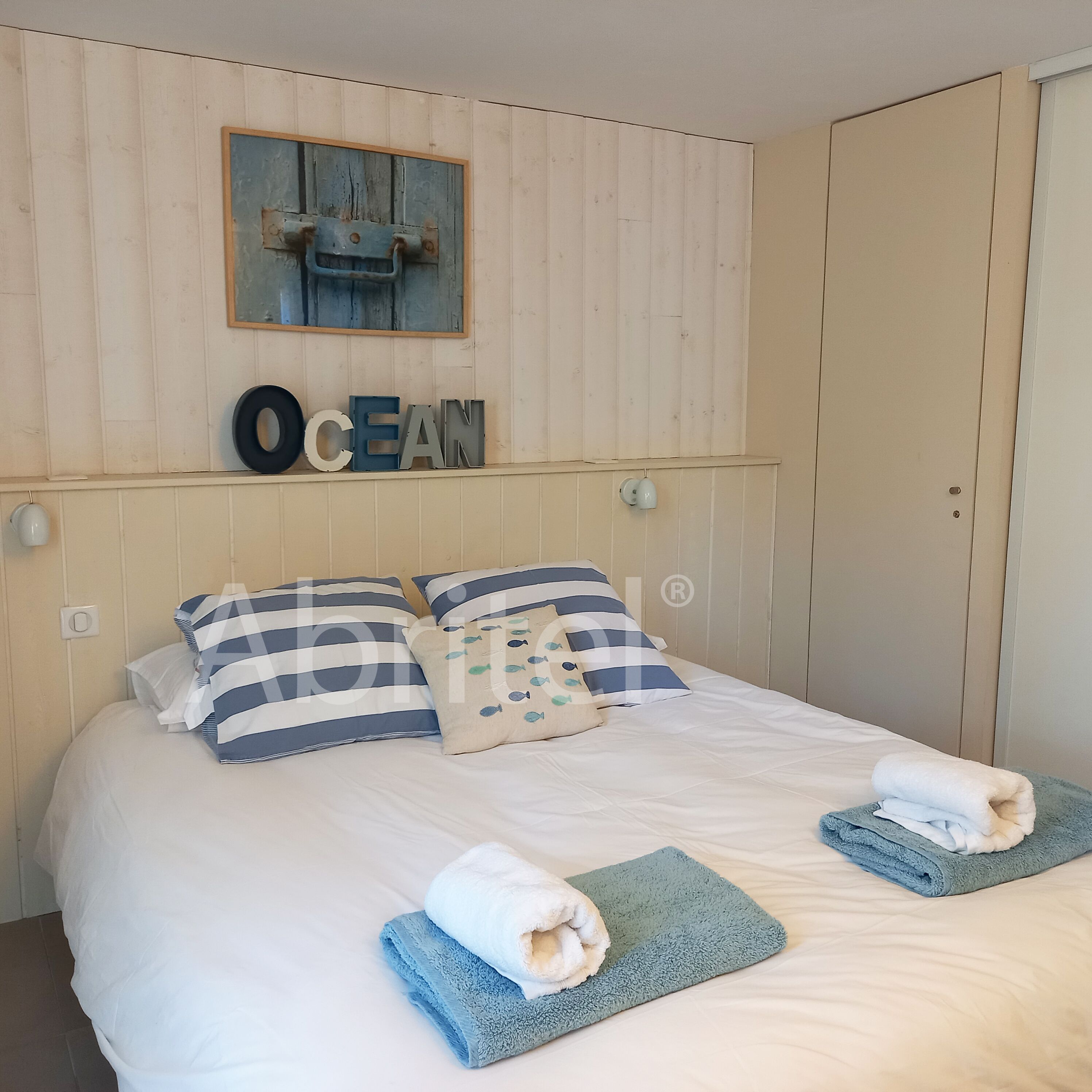 A neatly made bed with striped pillows, a small decorative item, and folded towels.