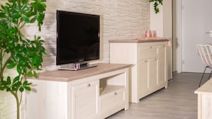 A modern living room with a flat-screen TV on a wooden cabinet, a potted plant, and a white brick wall. - Friendly, wheelchair-accessible vacation rental in Lengfurt: The Berger Family (Triefenstein)