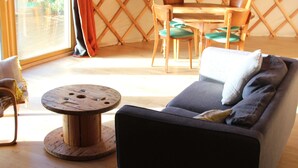 Een gezellige zithoek met een bank, een ronde houten tafel en een eethoek in een tentvormige constructie.