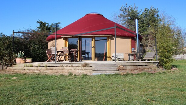 Een yurt-achtig gebouw met een rood dak, een glazen deur en een terras met buitenmeubilair.