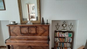 A wooden piano with a bench, a bookshelf with books, and a mirror on the wall.