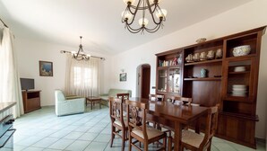 A spacious living room with a dining area, a kitchen, and a large wooden cabinet with decorative items.