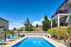 Ein Pool mit Liegestühlen, umgeben von Bäumen und Gebäuden.