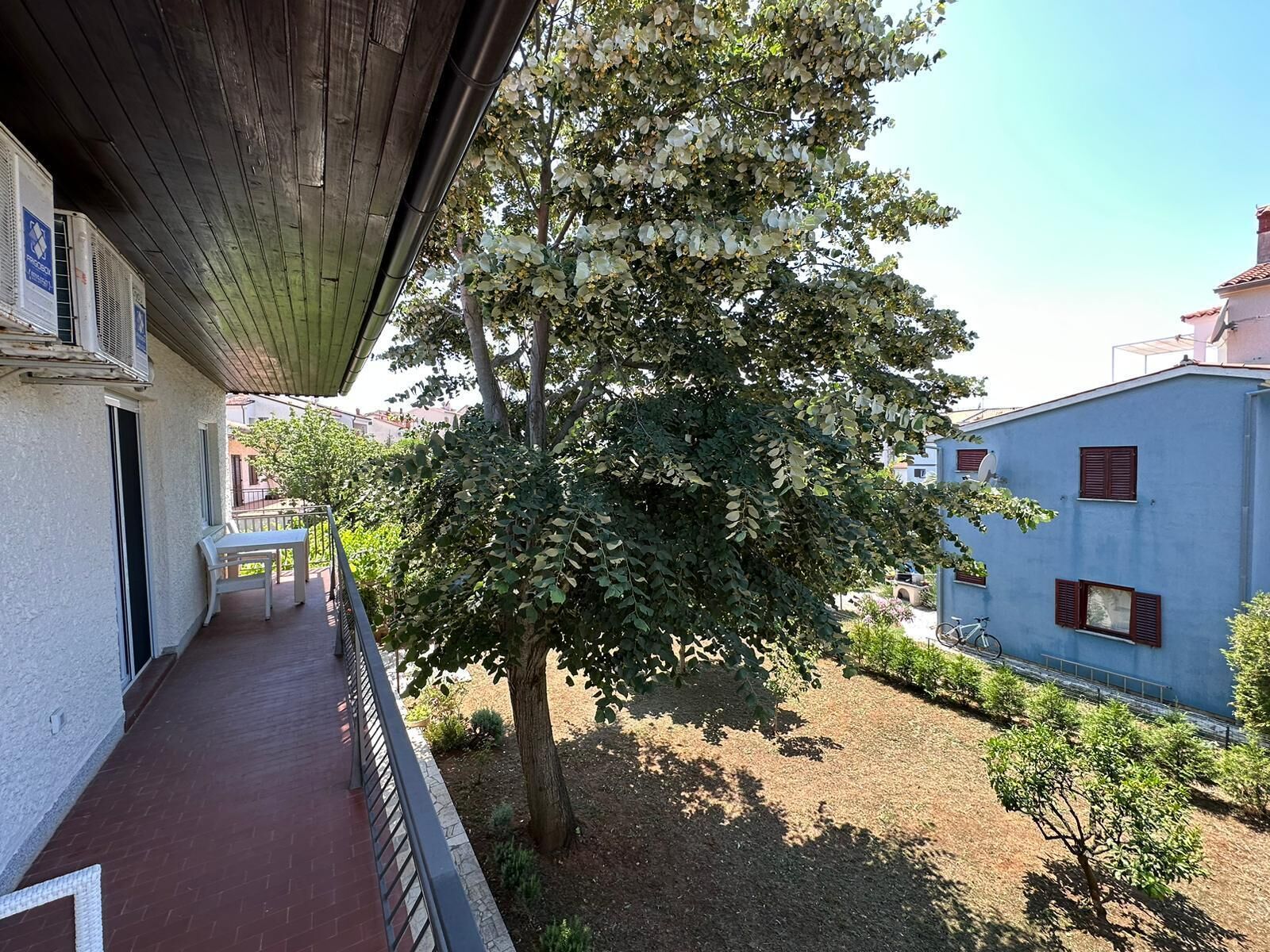 Un balcón con vista a un árbol y un edificio azul.