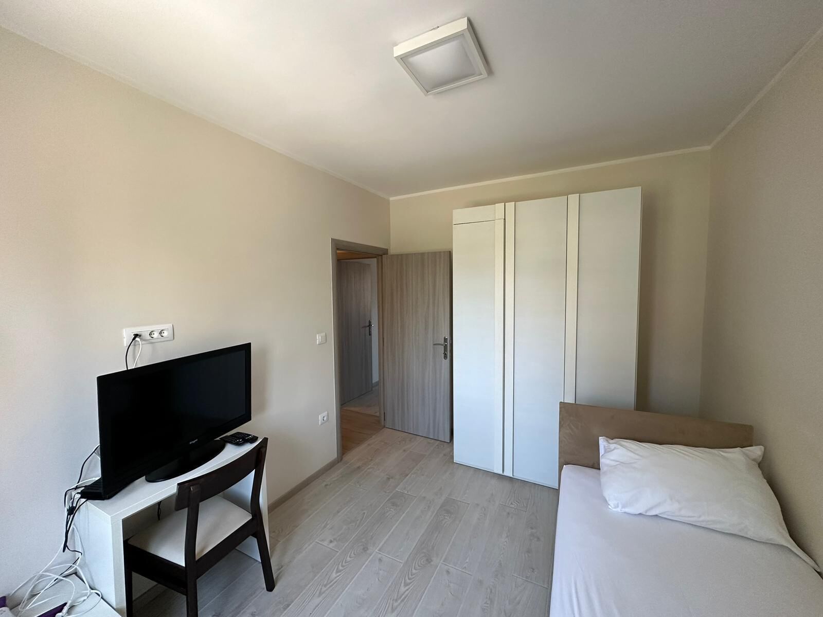 Een moderne hotelkamer met een flatscreen televisie op een bureau, een bed met wit beddengoed en een kledingkast met schuifdeuren.