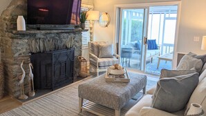 A living room with a stone fireplace, a television, and a view to the outside. - Cozy Waterfront Home In Portsmouth (Portsmouth)