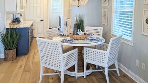 A dining area with a round table, white wicker chairs, a chandelier, and a view of the kitchen and living area. - Cozy Waterfront Home In Portsmouth (Portsmouth)