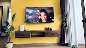 A living room with a yellow wall, a mounted TV, a wooden entertainment unit, and a potted plant.