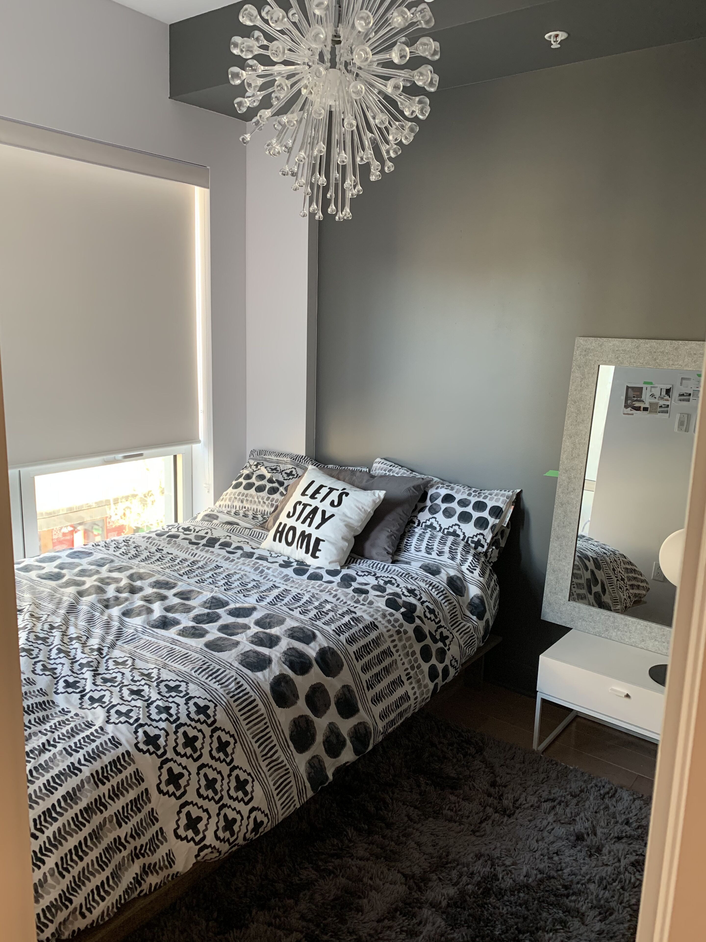 Une chambre à coucher moderne avec une couvre-lit à motifs, un luminaire décoratif au plafond et une table de chevet avec un miroir.