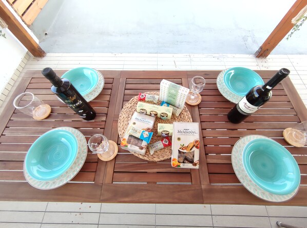 A wooden table with four turquoise plates, two wine bottles, and various packaged snacks and condiments. - Stegna Grand View (Stegna Beach - Rhodes)
