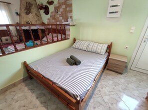 Habitación individual con una cama de madera, ropa de cama a rayas, una mesita de noche pequeña y piso de baldosas.