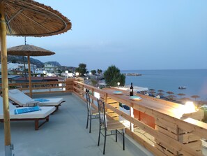 A terrace with wooden furniture, a table with wine glasses, and a view of the sea and buildings. - Stegna Grand View (Stegna Beach - Rhodes)
