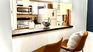 A modern kitchen with white cabinetry, a black countertop, and a brown chair. - Art and Foodie Lover`s Dream -Live Like a Local in Montrose (Houston)