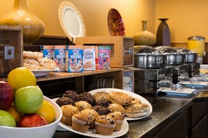Un bufé con diversos alimentos, como muffins, pasteles y cajas de cereales.
