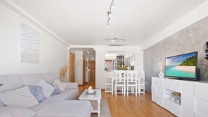 A modern living room with a sofa, a coffee table, a TV, and a dining area with chairs and a table. - Los Ranchos 4-3 Apartment Levante Beach (Benidorm)