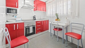 A compact kitchen with red cabinets, a microwave, a stove, and a small dining area with two chairs. - Los Ranchos 4-3 Apartment Levante Beach (Benidorm)