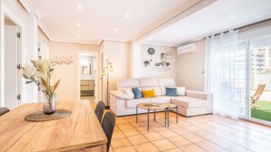A modern living room with a wooden dining table, a sofa, and a coffee table. There is a large window with a view of the outside. - Penthouse Ancla 562 Levante Beach (Benidorm)
