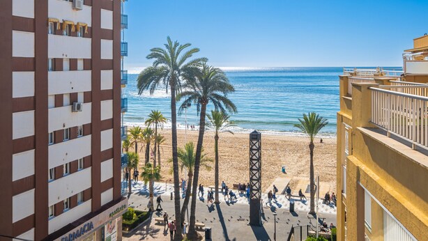 A high-rise building with a pharmacy on the ground floor, overlooking a beach with palm trees and people walking. - Penthouse Ancla 562 Levante Beach (Benidorm)