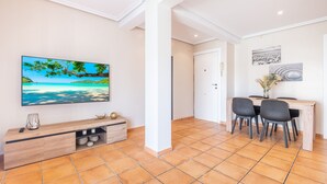 A modern living room with a flat-screen TV, wooden entertainment unit, dining table with chairs, and a tiled floor. - Penthouse Ancla 562 Levante Beach (Benidorm)
