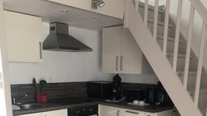 Een keuken met witte kastjes, een fornuis, een spoelbak en een trap.