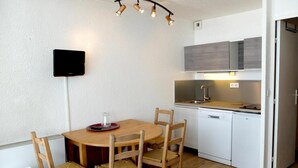 A compact kitchen with white cabinets, a wooden dining table with four chairs, and a built-in dishwasher. - 100m from resort center, balcony, tv, ski locker, 21m², Tignes (Tignes)