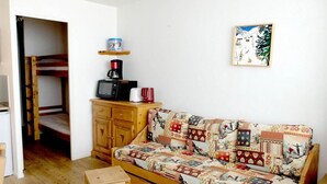 A cozy room with a wooden sofa, a small wooden table, a cabinet with a coffee maker, and a bunk bed in the background. - 100m from resort center, balcony, tv, ski locker, 21m², Tignes (Tignes)