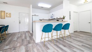 A modern kitchen with white cabinets, a wooden countertop, and teal bar stools. - 2BR Mickey Magic Condo | Family Stay Near Disney + Pool (Kissimee)