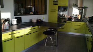 A modern kitchen with yellow cabinets, a black countertop, and stainless steel appliances. There is a bar stool and a window providing natural light. - 3-star Villa Nelson sleeps 6 3 bedrooms private pool (Moliets-et-Maa)