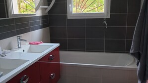 A modern bathroom with a white bathtub, red vanity, and a window with a view of greenery. - 3-star Villa Nelson sleeps 6 3 bedrooms private pool (Moliets-et-Maa)