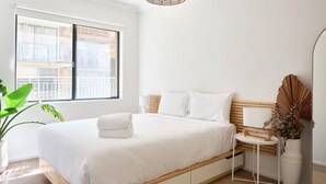 A modern bedroom with a large bed, a bedside table, a lamp, and a view of the outside.