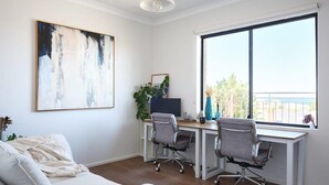 A modern office space with a white couch, two office chairs, a desk, and a large window with a view of greenery.