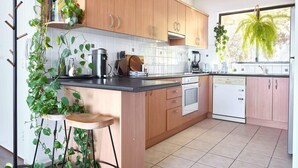 A kitchen with wooden cabinets, a black countertop, and a dishwasher. There are plants on the counter and a window with a view of trees.
