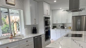A modern kitchen with white cabinets, stainless steel appliances, and a marble countertop. - PARADISE BY THE BEACH AND YOUR OWN PRIVATE POOL (West Palm Beach)