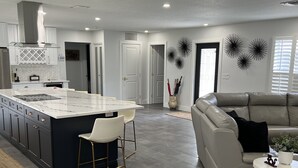 A modern kitchen with a central island, bar stools, and a dining table. There is a living area with a sofa and a coffee table. - PARADISE BY THE BEACH AND YOUR OWN PRIVATE POOL (West Palm Beach)